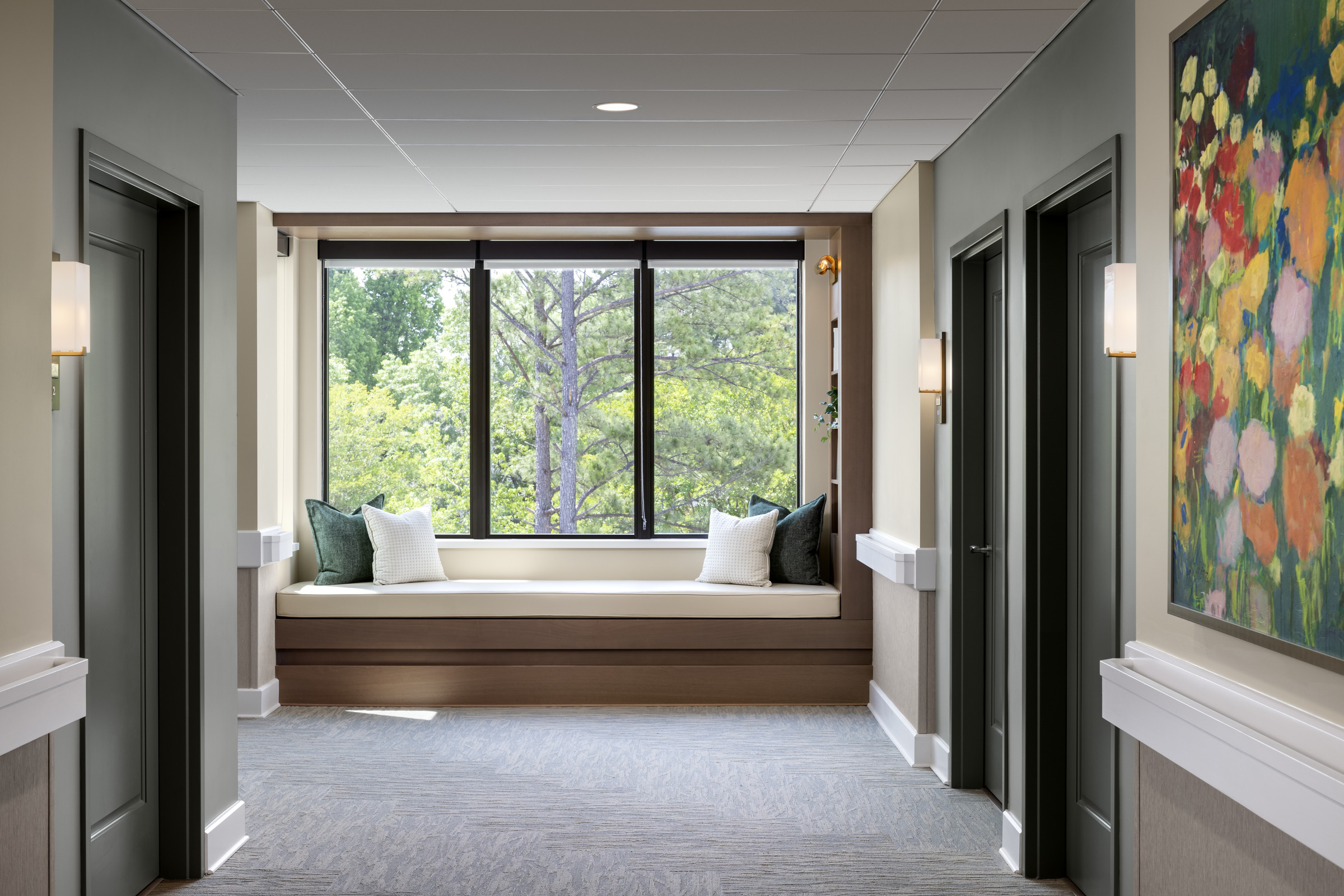 National Assisted Living Week Profile: The Forest at Duke. This image shows a large window seat at the end of the corridor, looking out to the forested campus. 